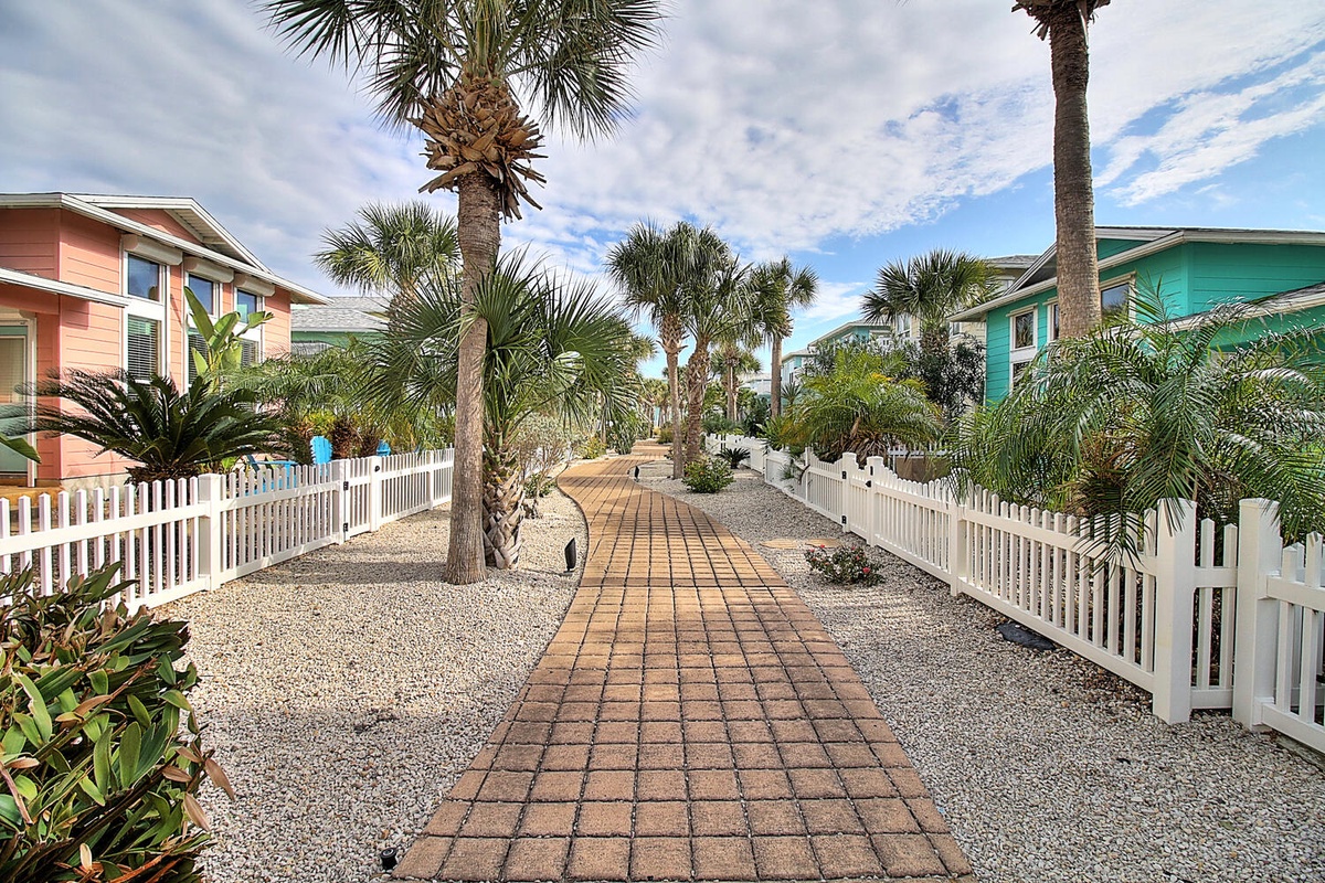 Charming coastal neighborhood featuring colorful beach homes and tropical palms along a welcoming brick walkway.