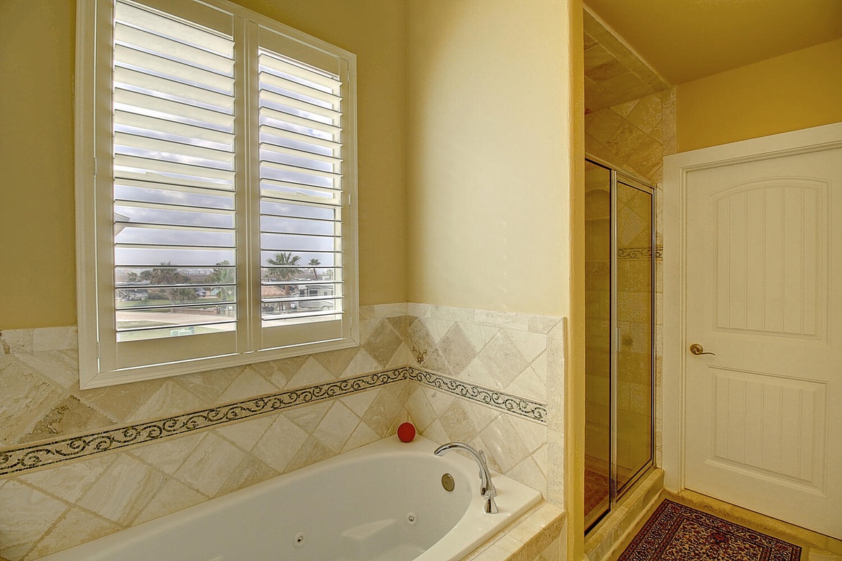 Unwind in your elegant bathroom featuring a luxurious soaking tub and separate glass shower, all bathed in warm golden light.