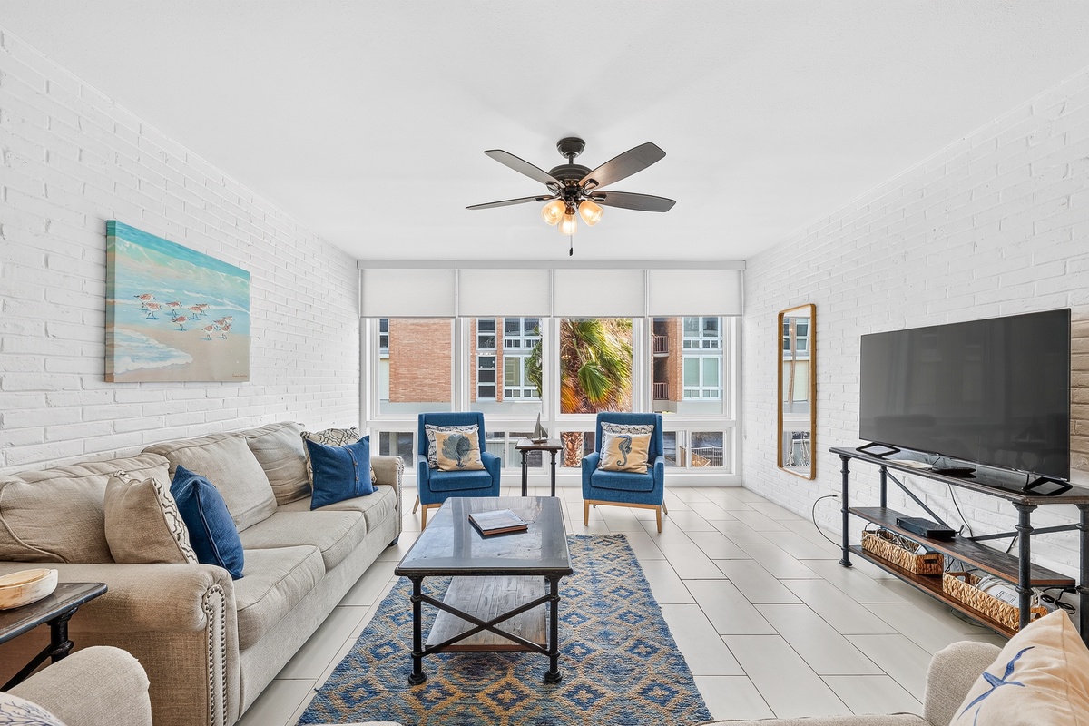 Relax into coastal comfort with plush seating, cool tile floors, and a gentle breeze from your ceiling fan. Two inviting chairs frame your window, perfect for sipping morning coffee or unwinding after a beach day.