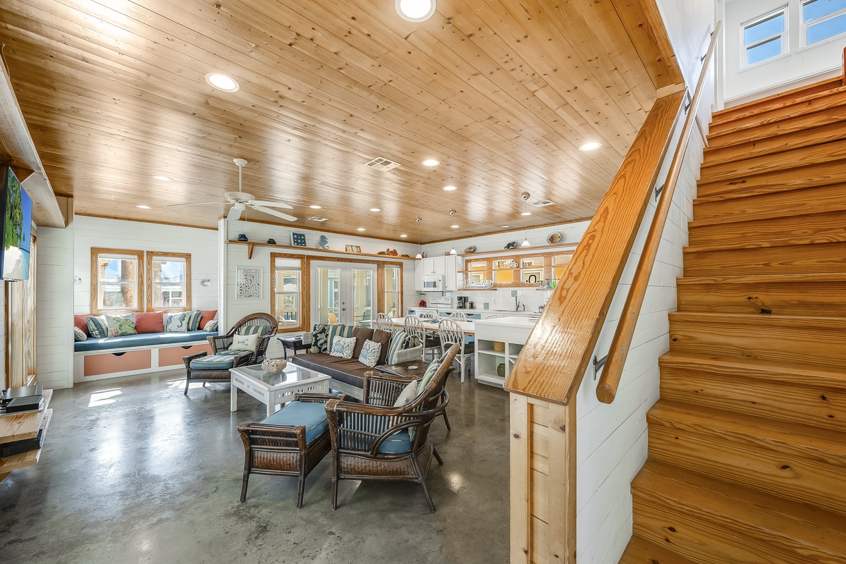 Relax in your spacious open-concept living area with warm wood ceilings, comfortable seating, and modern kitchen nearby.