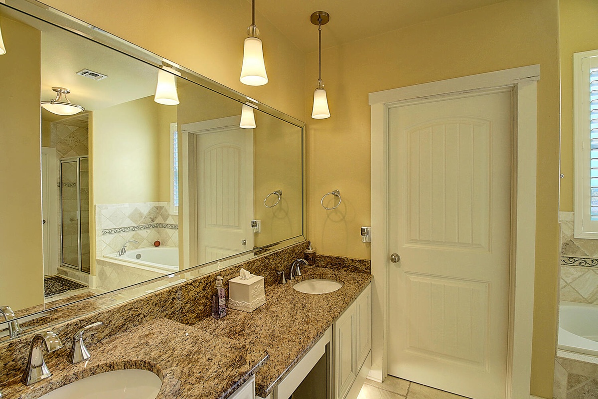 Unwind in your elegant bathroom featuring dual granite vanities, ambient pendant lighting, and a luxurious soaking tub for ultimate relaxation.