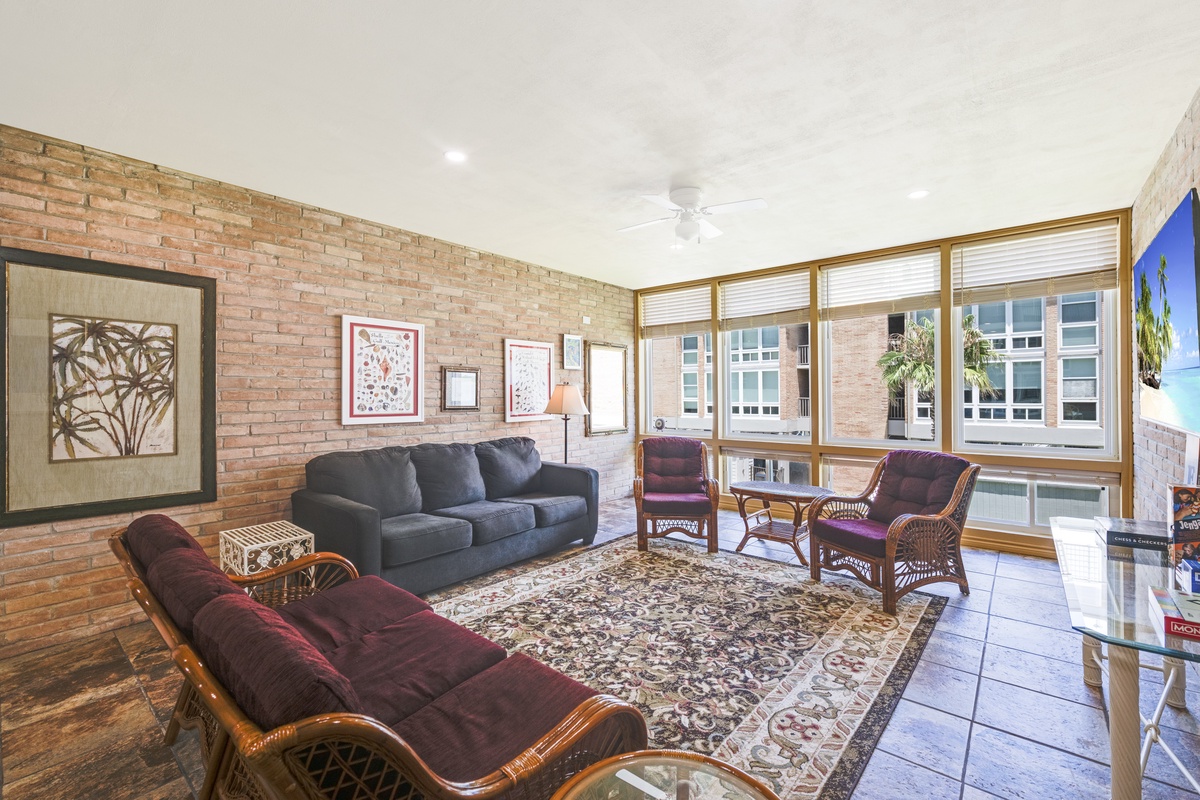 Settle into this inviting living space with warm brick accents, comfortable seating, and large windows flooding the room with natural light—your perfect home away from home.