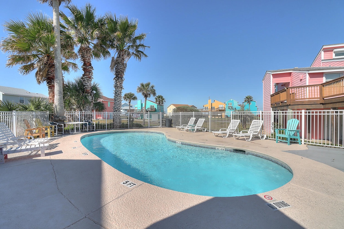 Sparkling pool surrounded by swaying palms and colorful coastal cottages, inviting you to relax under sunny skies in this tropical oasis.