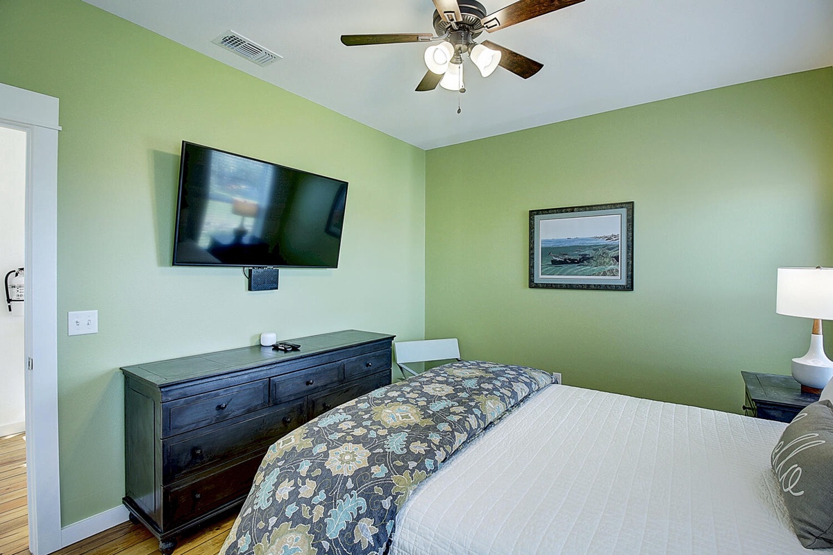 Relax in your peaceful bedroom with soothing green walls, comfortable linens, and modern amenities like a flat-screen TV and ceiling fan for perfect comfort.