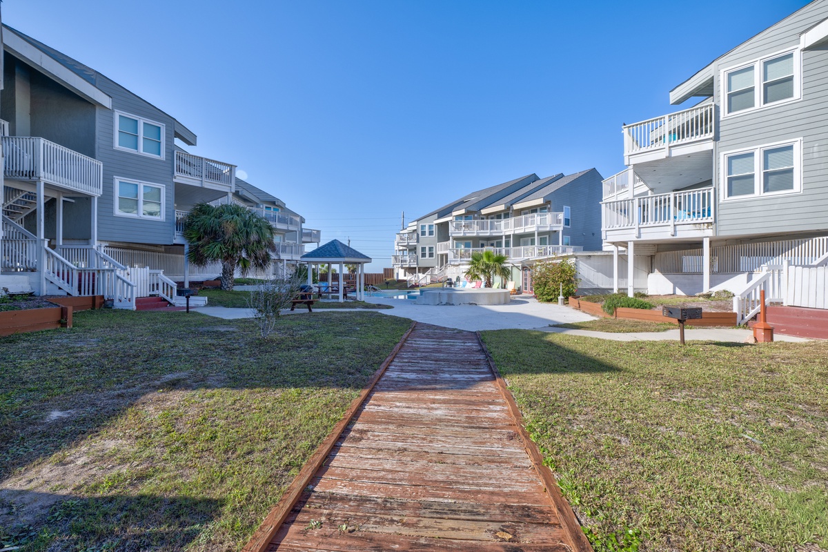 Coastal vacation rental community featuring multiple beach houses with balconies and a central pool area surrounded by tropical landscaping.