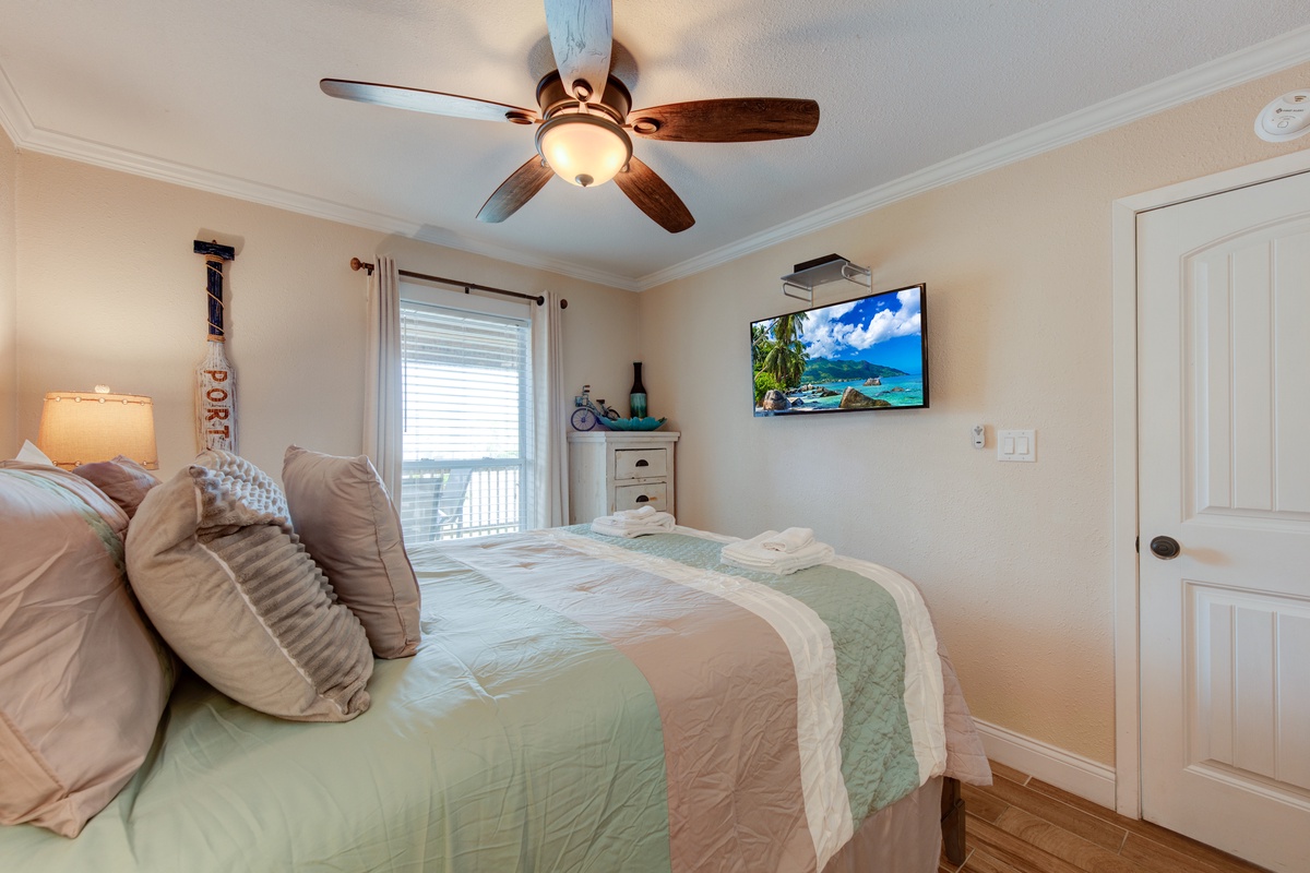 Your coastal bedroom awaits with soft linens, overhead fan, and tropical views on the mounted TV to set your vacation mood perfectly.