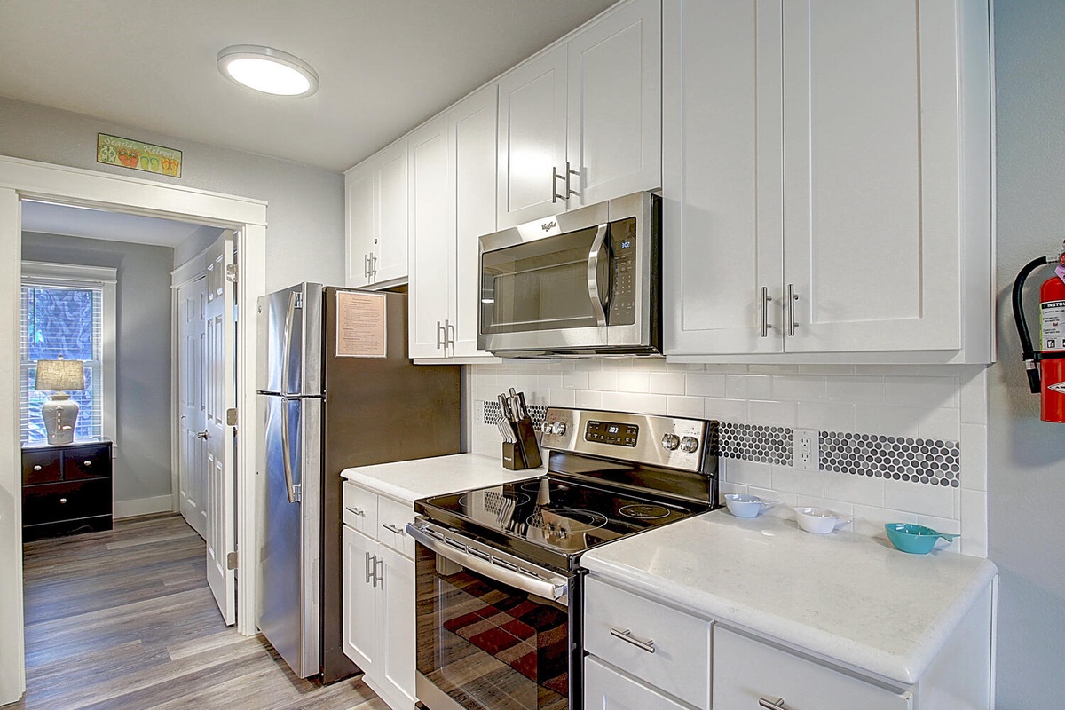 Your bright, fully-equipped kitchen features crisp white cabinetry, modern stainless appliances, and ample counter space for preparing meals.