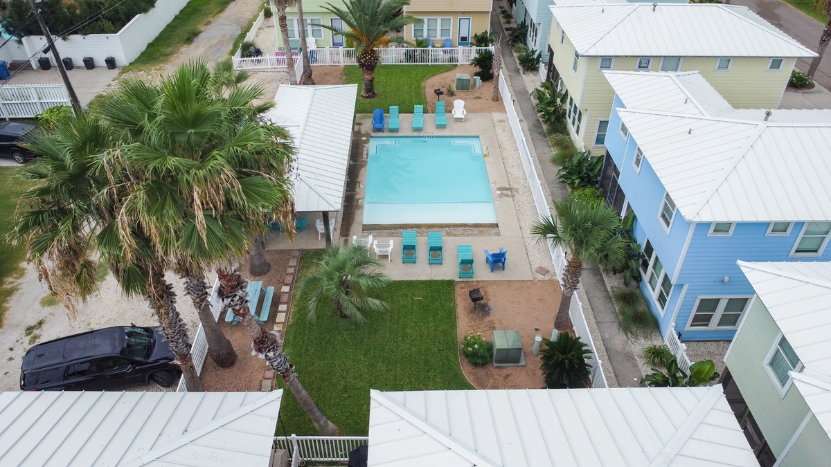 Aerial view of tropical vacation rental community with central swimming pool, palm trees, and colorful beach houses.