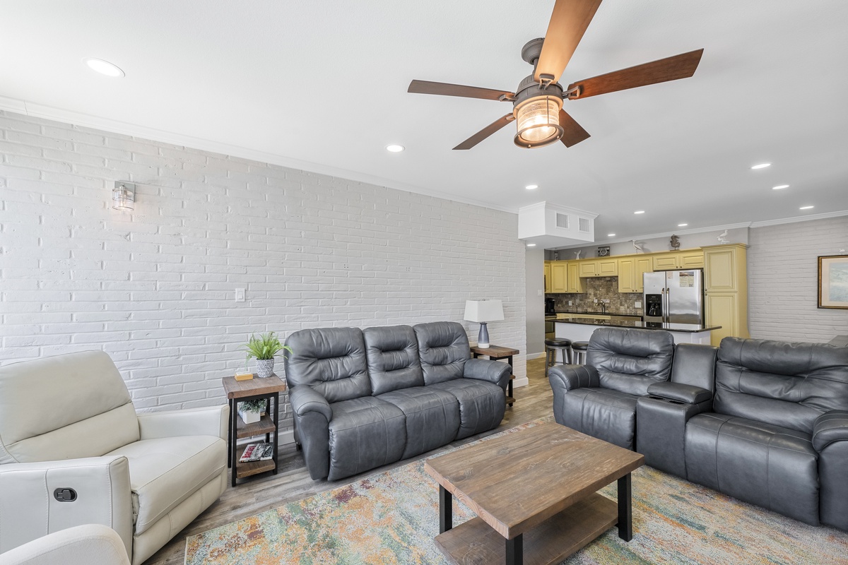 Relax in your spacious living room featuring comfortable leather recliners, modern brick accent wall, and charming ceiling fan.