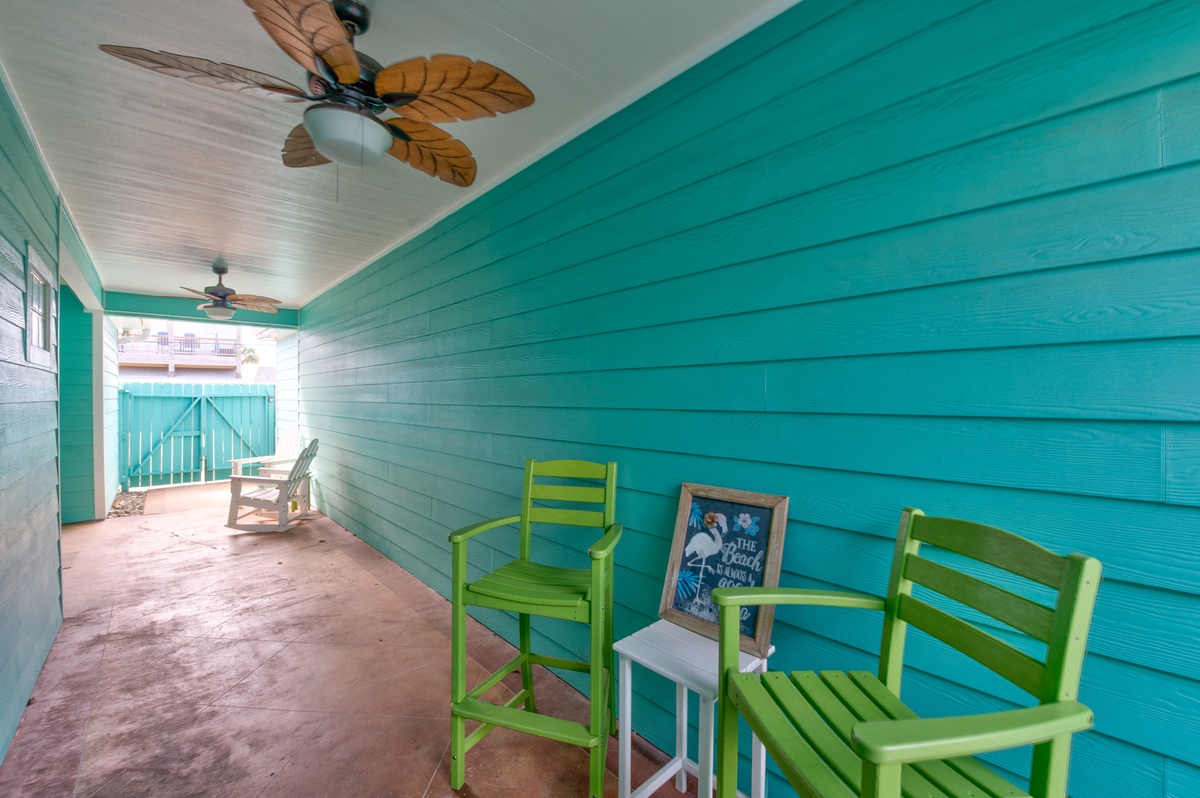 Your covered porch offers tropical charm with turquoise walls, palm-blade ceiling fans, and colorful seating perfect for morning coffee or evening relaxation.