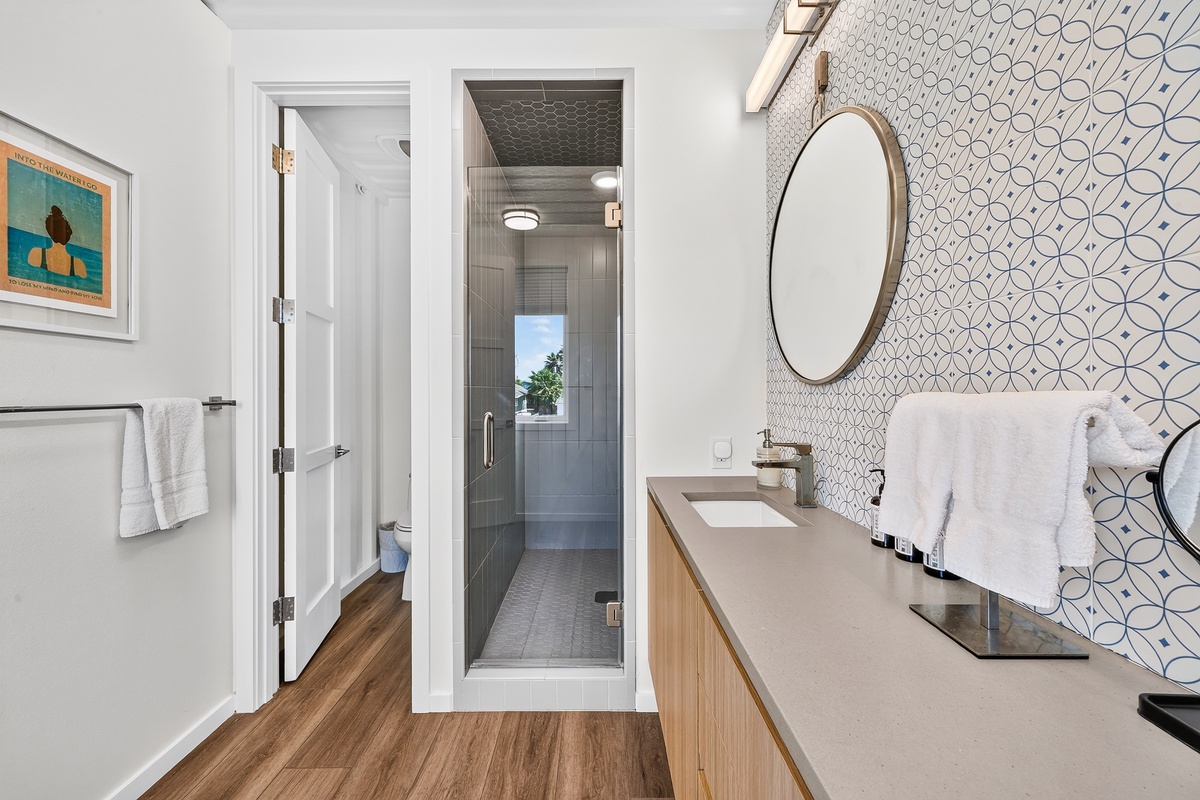 Step into your primary bathroom, where modern tile meets warm wood accents. Fresh towels await you, and the sleek walk-in shower is perfect for refreshing after a day of exploring.