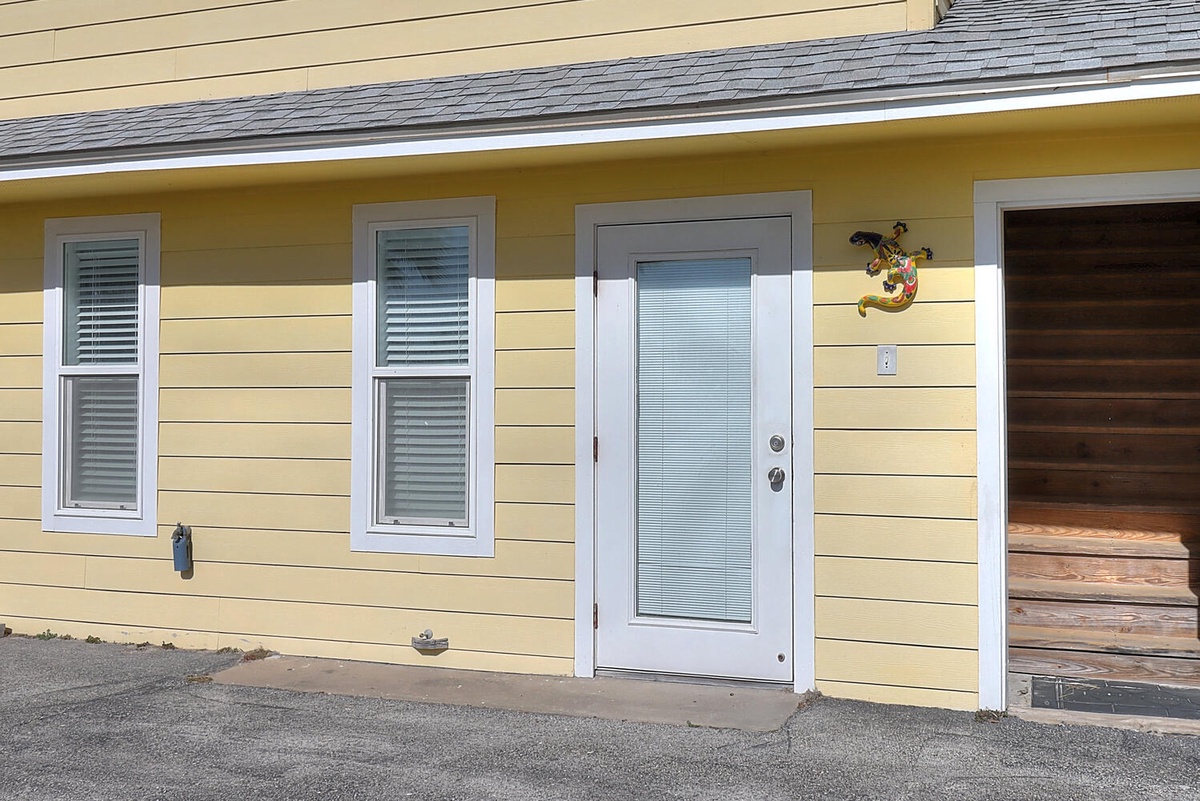 Charming yellow cottage entrance with white trim and convenient parking, welcoming you to your coastal retreat.