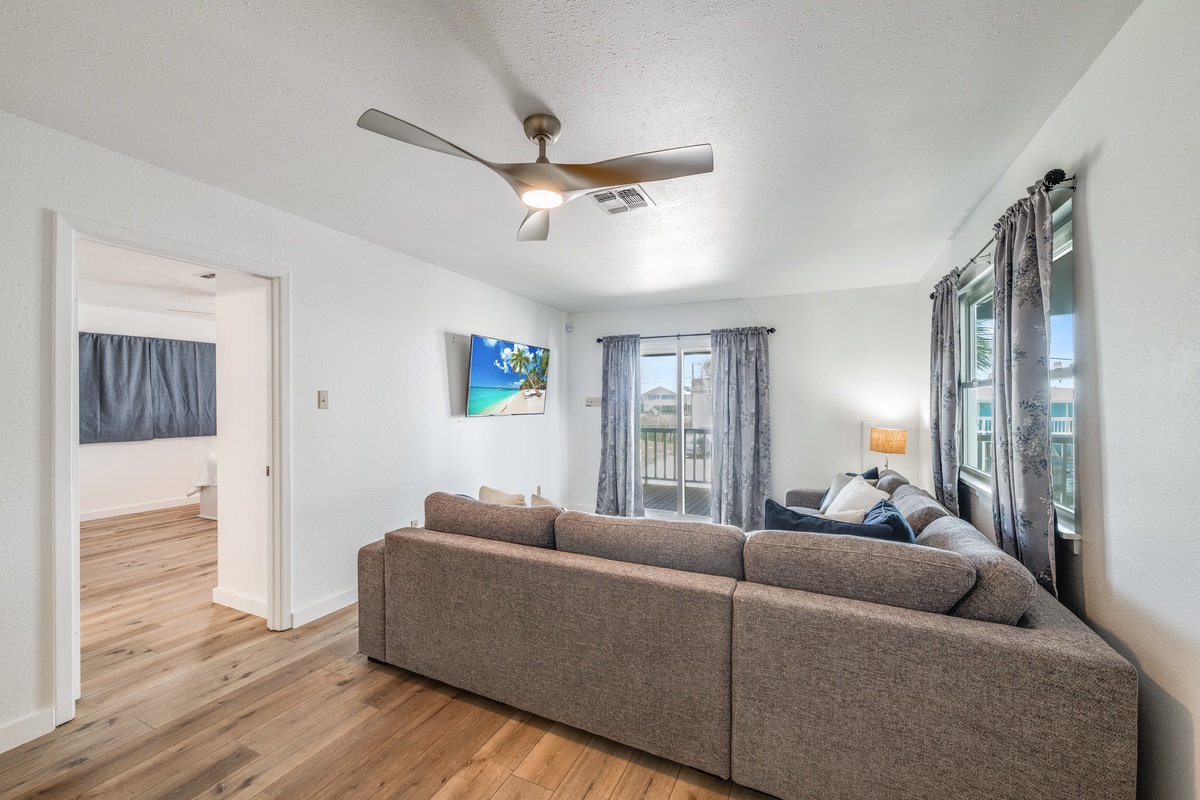 Relax in your bright living room with plush sectional seating, ceiling fan, and wall-mounted TV for cozy evenings.