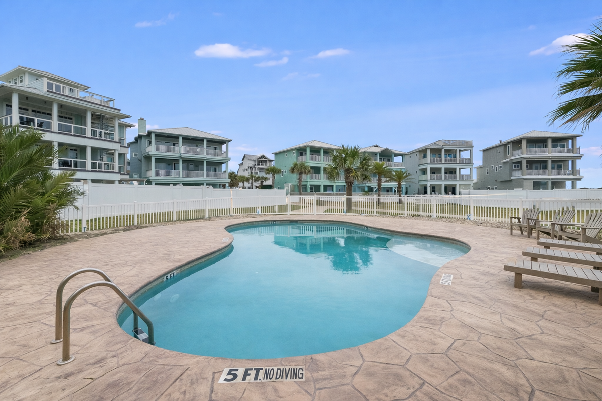 Oceanfront vacation rental community with kidney-shaped pool, loungers, and palm-lined boardwalk entrance.