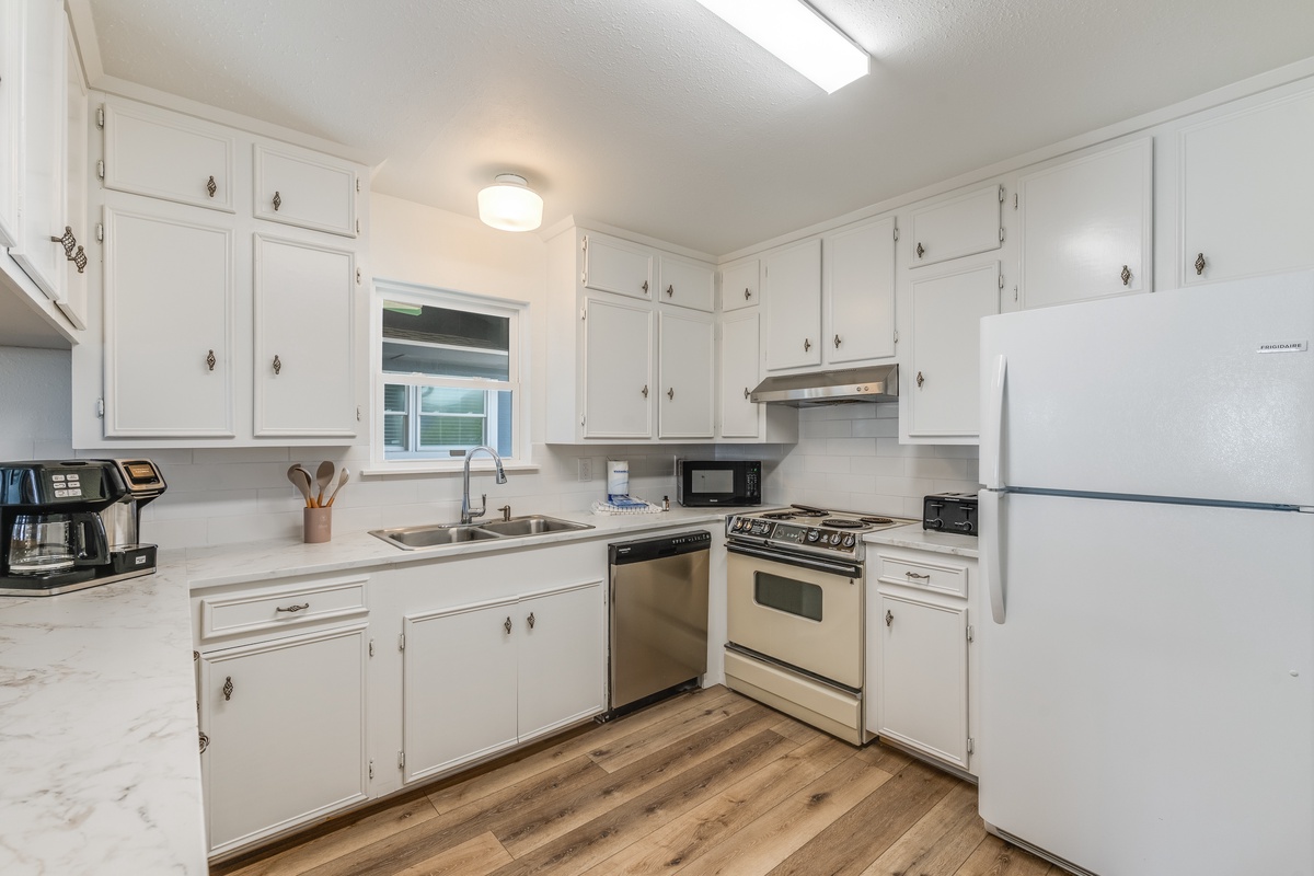 Your bright, fully-equipped kitchen awaits with white cabinets, stainless appliances, and warm wood floors.