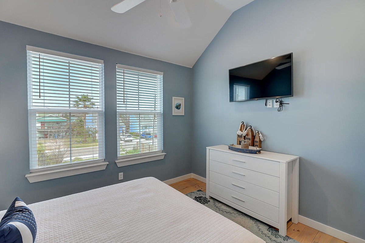Relax in your serene bedroom with calming blue walls, crisp white linens, and a wall-mounted TV for cozy evenings in.