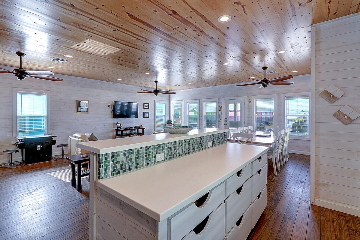 Your spacious open kitchen flows seamlessly into the dining area, where warm wood ceilings and coastal-inspired finishes create the perfect gathering space.