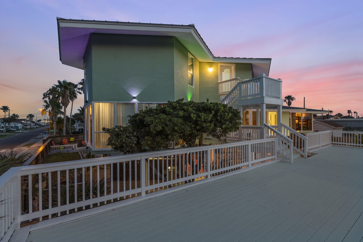 Modern beachfront architecture glows against a stunning sunset backdrop, featuring multiple levels and spacious outdoor decking.