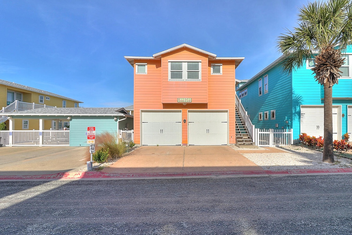 Bright orange beach house with garage parking stands among colorful coastal homes in this vibrant neighborhood.
