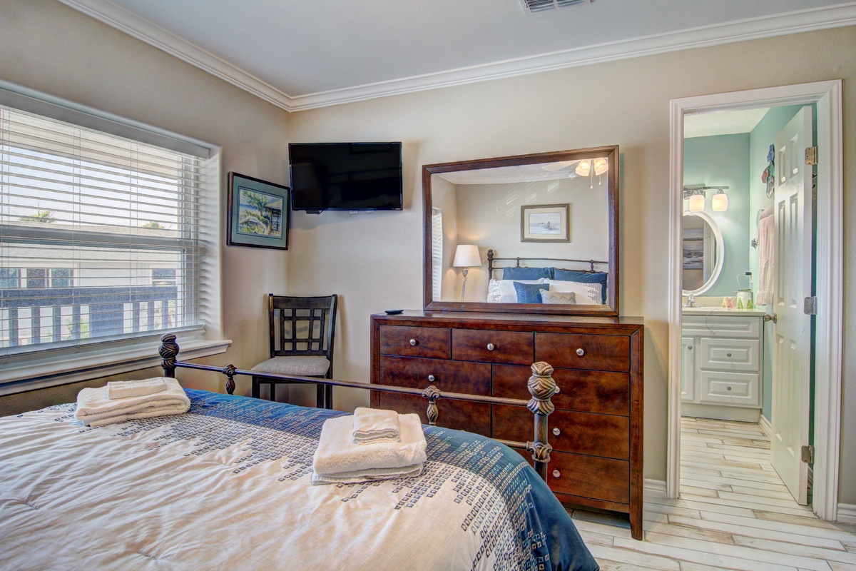 Your elegant bedroom features a plush bed with fresh linens, warm wood furnishings, and a wall-mounted TV for relaxation.