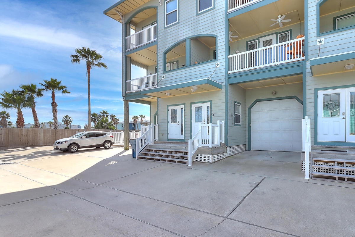 Modern coastal property with multiple levels of covered balconies, convenient parking, and tropical palm trees surrounding the entrance area.