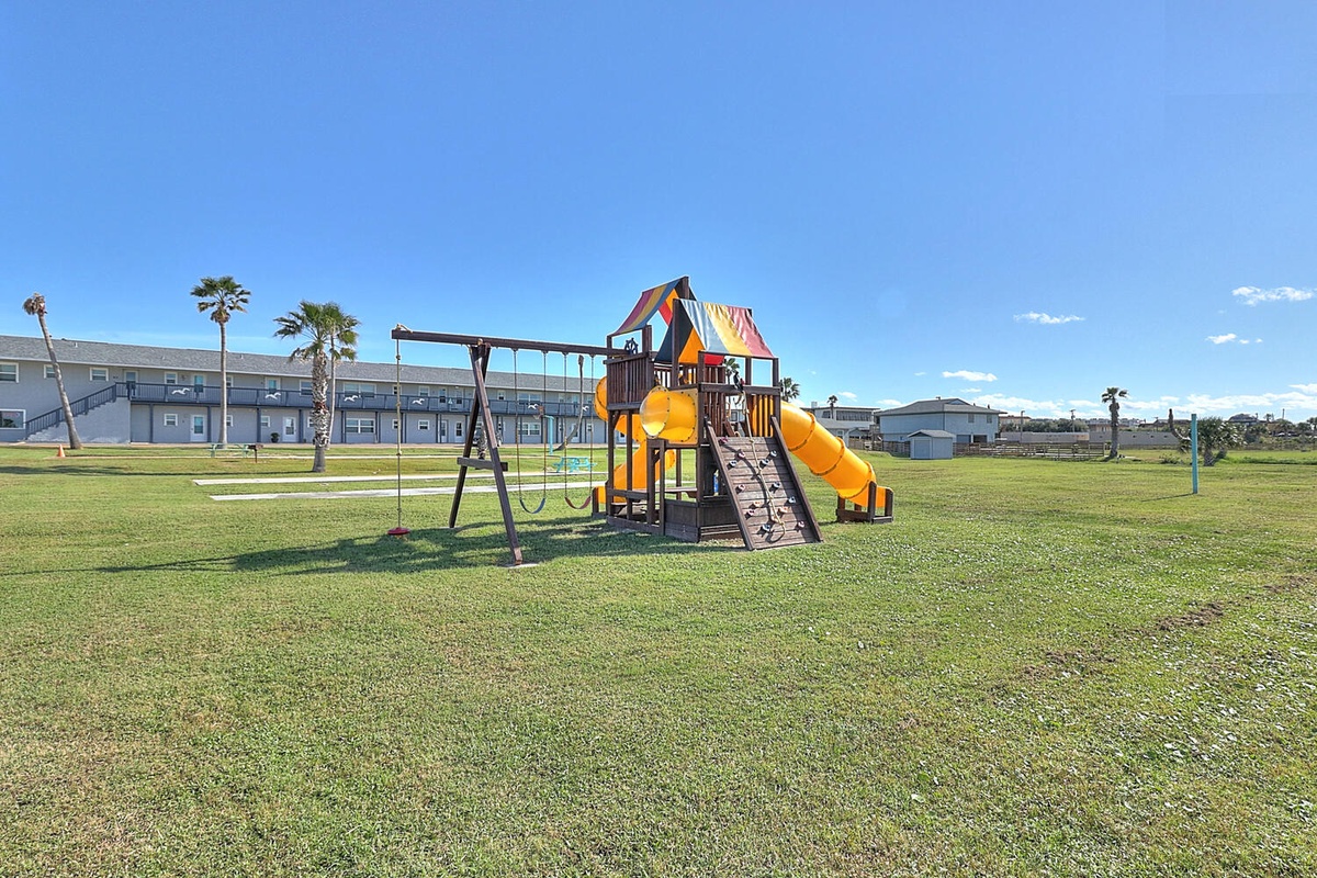 Spacious playground with colorful slides and swings sits in the open green area near the property buildings.