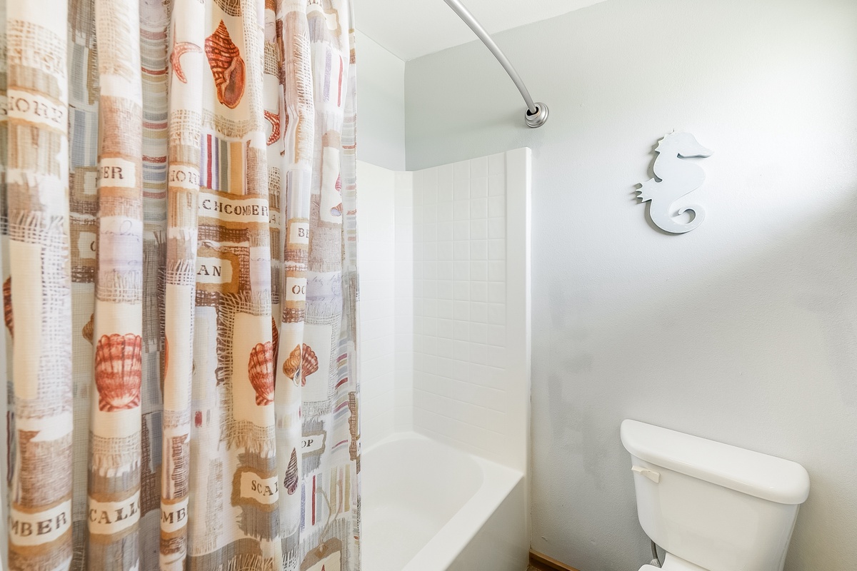 Step into your clean, nautical-themed bathroom with a relaxing tub-shower combo and charming seashell curtain.