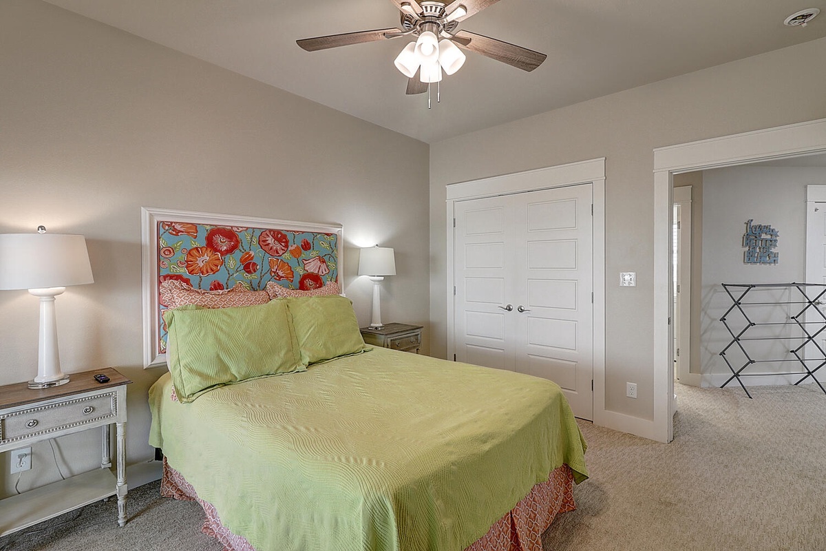 Drift off in this bright bedroom with colorful floral headboard, soft green linens, and gentle ceiling fan breeze.