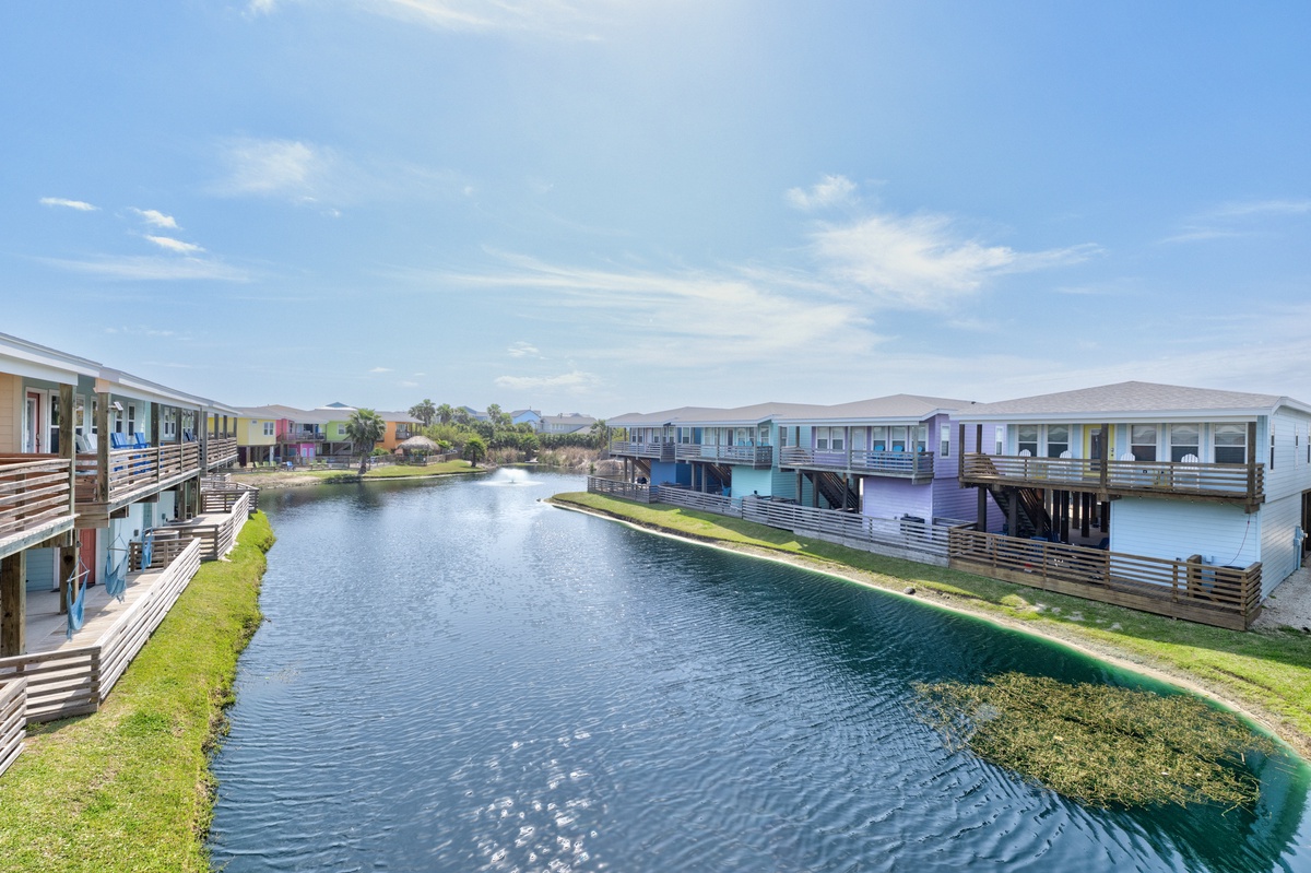 Colorful waterfront vacation rentals surround a peaceful canal with elevated decks and mountain views in the distance.