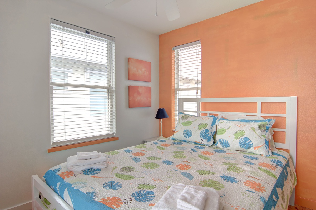 Wake up refreshed in your bright bedroom with tropical bedding and cheerful coral accent wall creating a cozy coastal retreat.