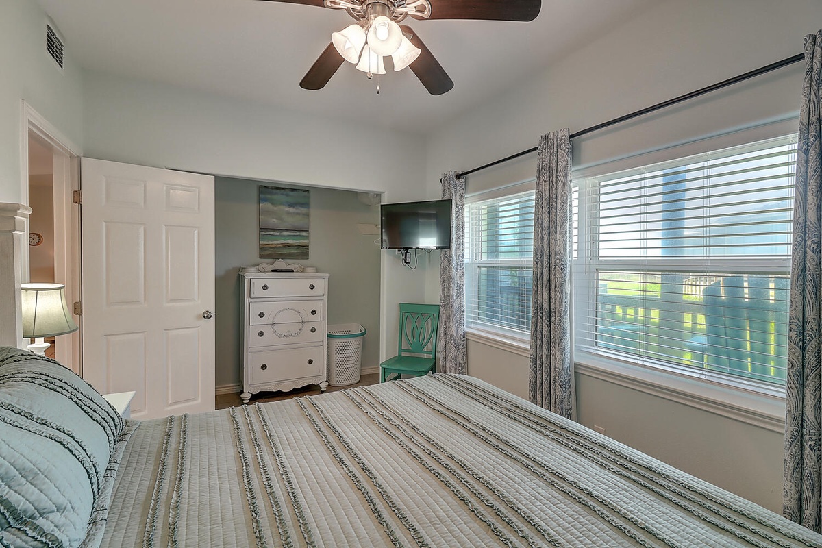 Rest peacefully in your airy bedroom with ocean-themed decor, ceiling fan comfort, and large windows filling the space with natural light.