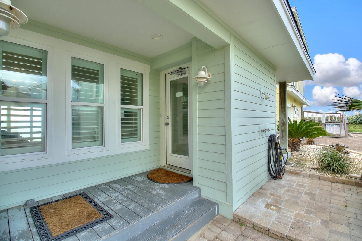 Charming coastal entrance with mint green siding and covered porch welcomes guests to this beachside retreat.