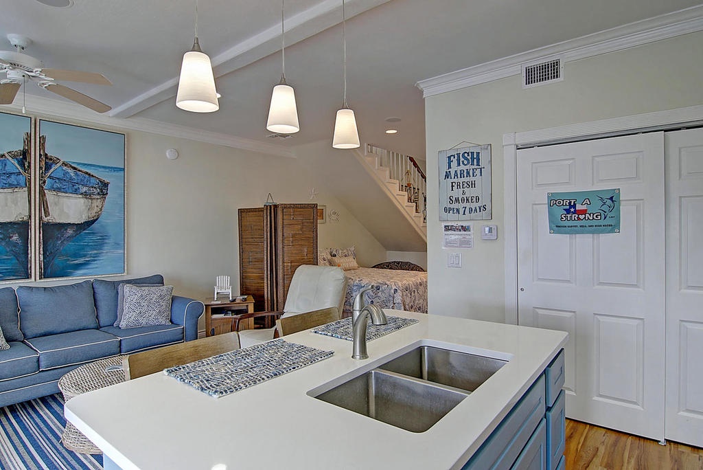 Your open kitchen flows into a coastal living room where nautical art meets modern comfort beneath elegant pendant lighting.