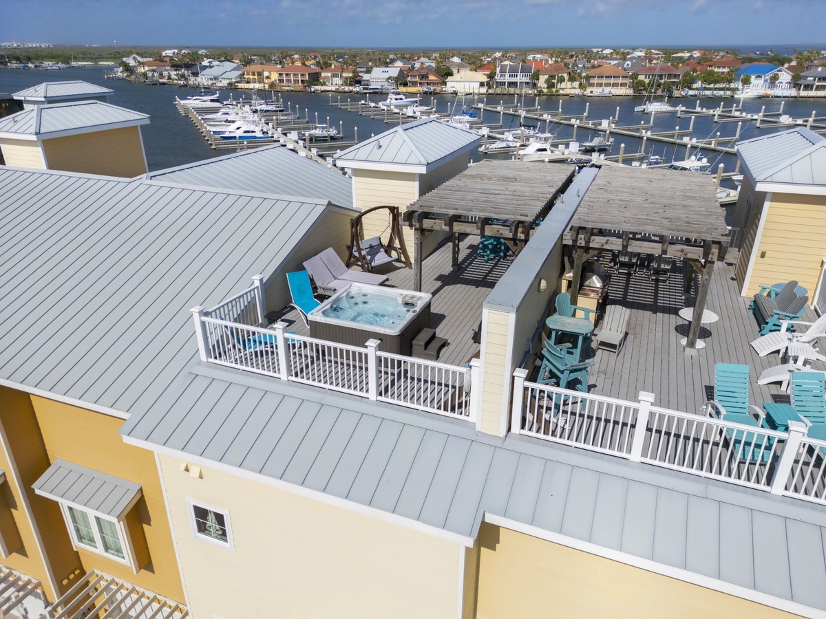 Aerial view showcasing the property's rooftop deck with hot tub, pergola seating areas, and marina backdrop.