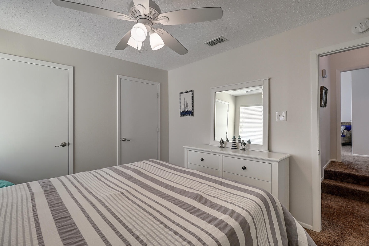 Rest peacefully in this serene bedroom with comfortable bedding, ceiling fan for cool breezes, and convenient storage.