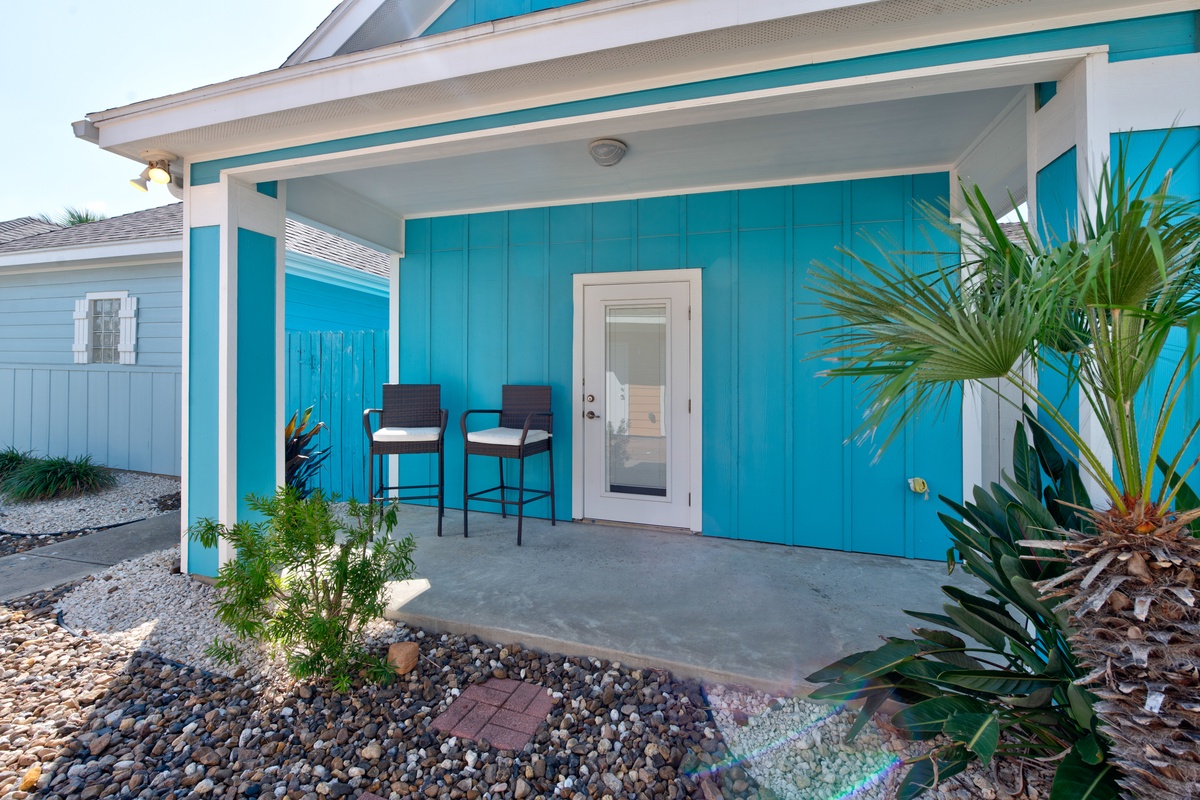 Bright turquoise cottage with covered porch and tropical plants creates a cheerful coastal welcome.