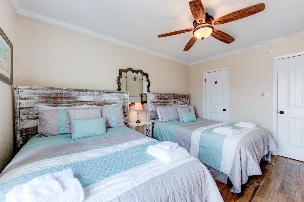 Drift off in coastal comfort with matching beds, weathered wood headboards, and soothing sea-glass linens beneath your own ceiling fan.
