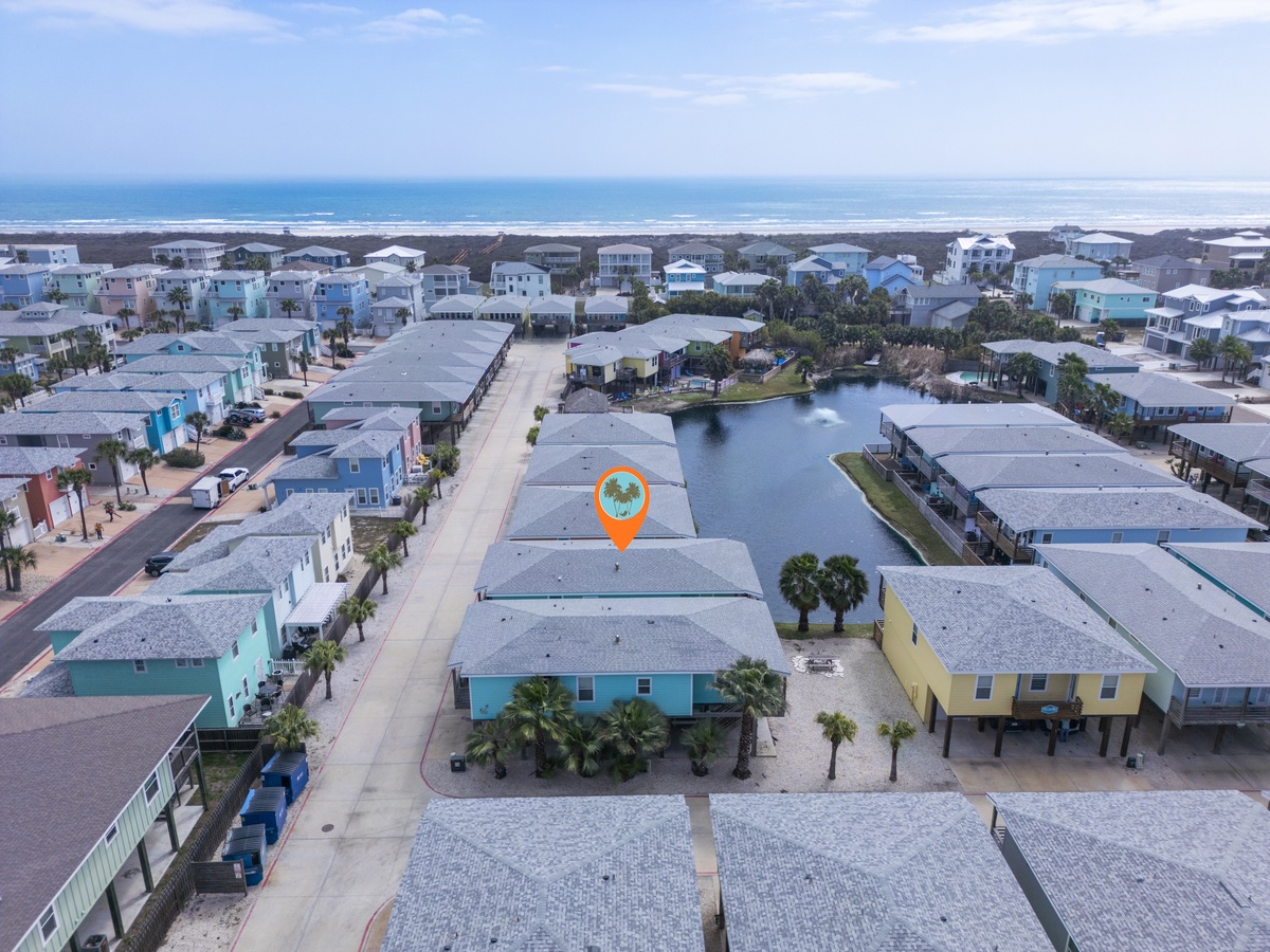 Aerial view of a coastal community with canal-front homes nestled between palm trees and the ocean, offering a peaceful neighborhood setting.
