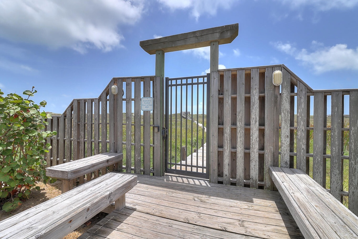 Wooden observation deck with safety railings overlooks natural landscape under blue sky with white clouds.