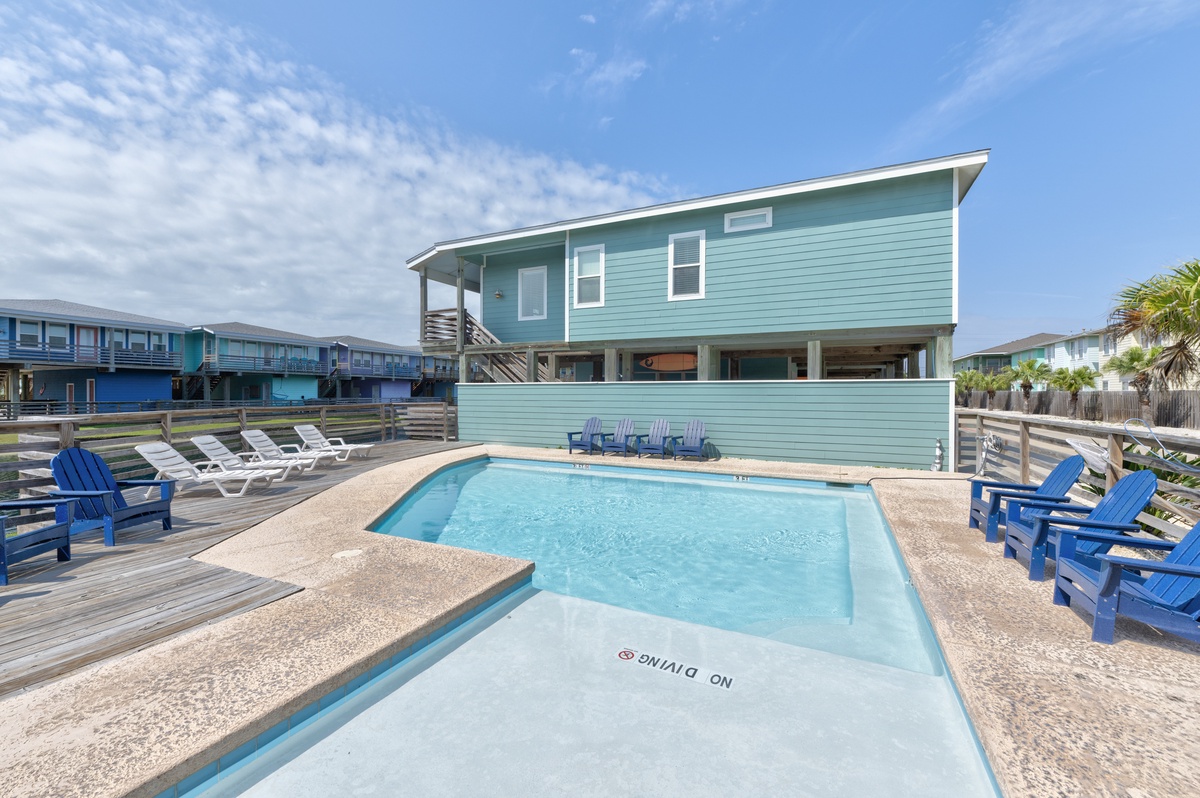 The property features a private pool surrounded by comfortable lounge chairs and bright blue Adirondack seating, perfect for sunny days and outdoor relaxation.