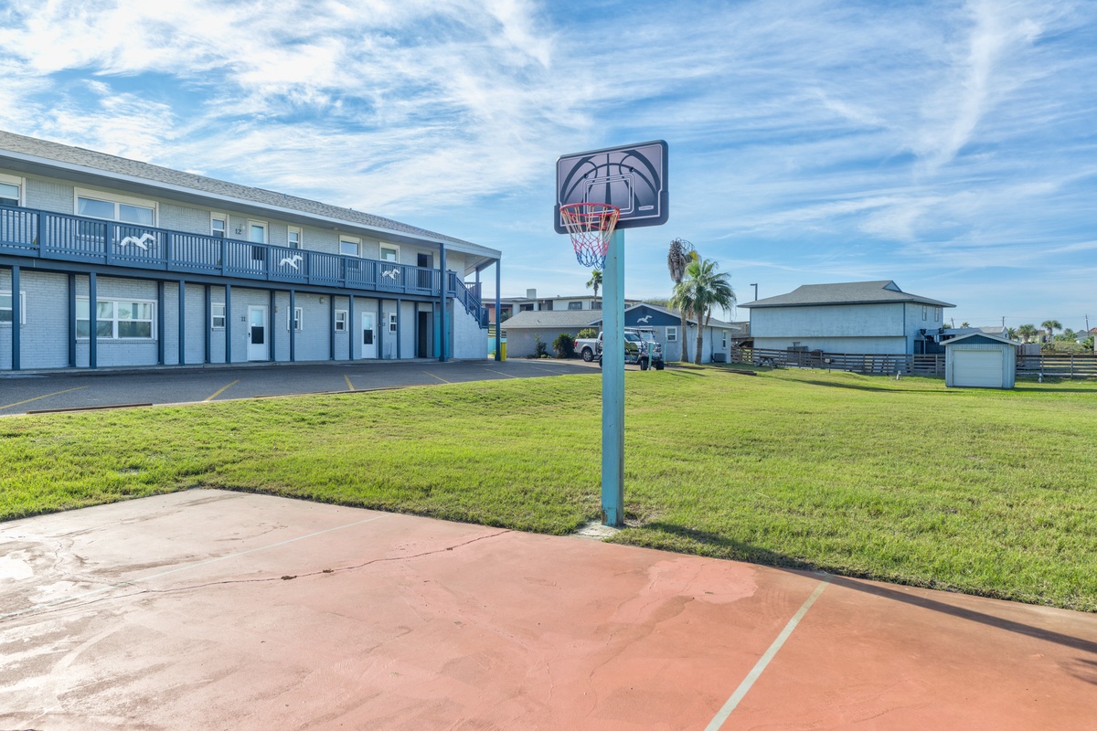 Beachfront property with basketball court, lawn area, and blue sky backdrop for active coastal getaways.