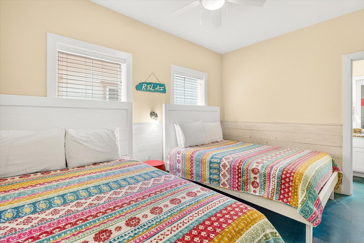 Relax in this cheerful twin bedroom with colorful quilts, natural light, and beachy vibes perfect for your coastal getaway.