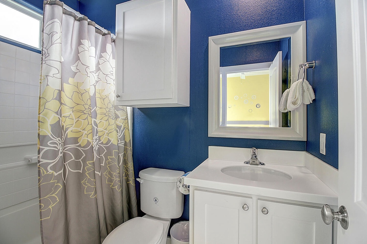 Your bright bathroom features crisp white fixtures against bold blue walls, with cheerful floral curtains adding warmth to your daily routines.