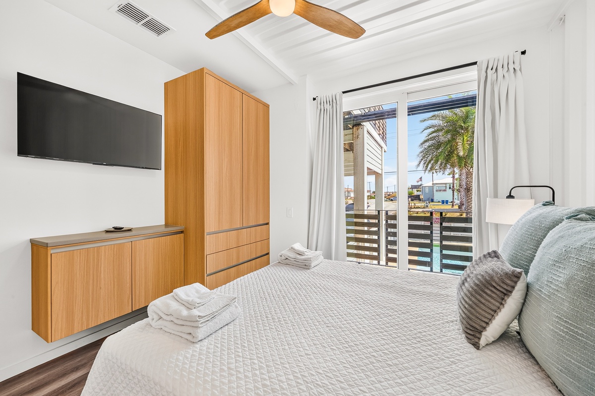 Slip into your third bedroom retreat where crisp white walls meet warm wood tones. Through the glass doors, palm trees sway and sunshine beckons you to unwind in your own waterside escape.