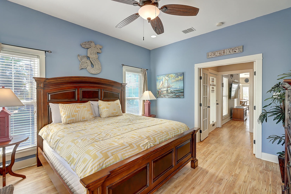 Your coastal bedroom sanctuary features soothing blue walls, rich wood furnishings, and cheerful yellow bedding beneath a gentle ceiling fan breeze.