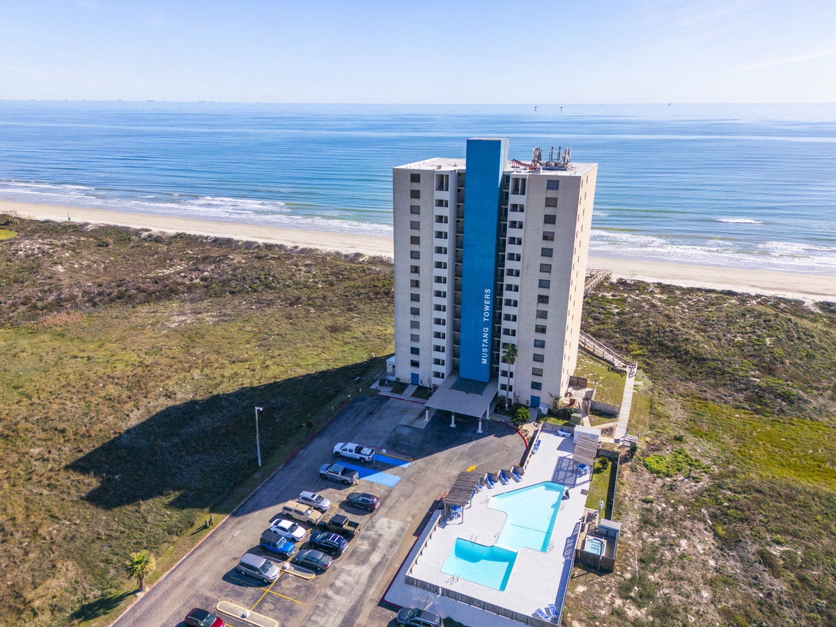Modern beachfront tower with pool and parking, nestled between pristine coastline and natural dunes.