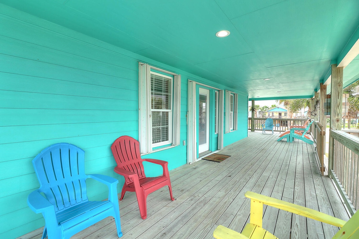Relax on your vibrant covered porch with colorful beach chairs overlooking the coastal neighborhood - the perfect spot to unwind.