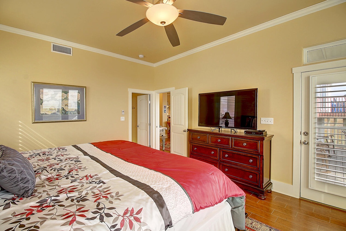 Your master bedroom features a ceiling fan, elegant dresser with TV, and warm natural light streaming through the windows for perfect relaxation.