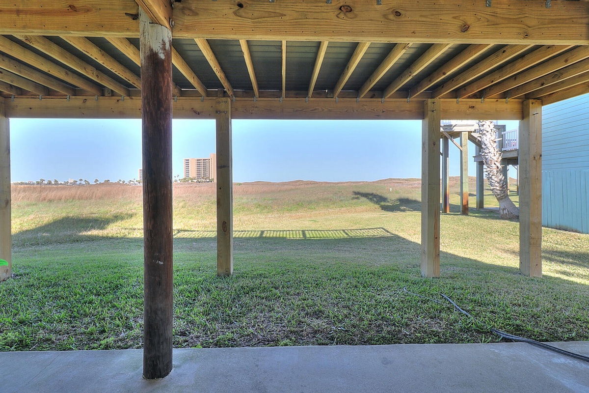 Covered outdoor space offering shade while you enjoy views of coastal dunes and distant beachfront buildings.