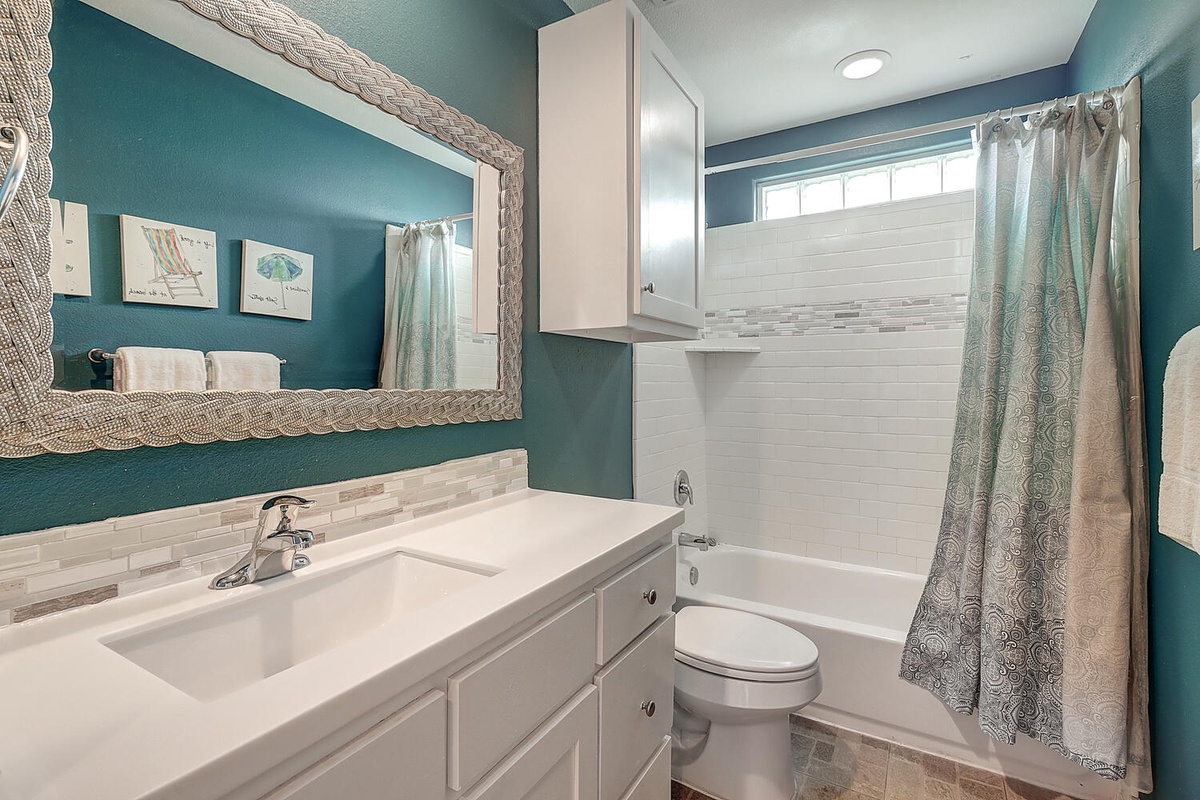 Refresh in your beautifully appointed bathroom featuring soothing teal walls, modern white vanity, and a relaxing tub-shower combo with designer touches.